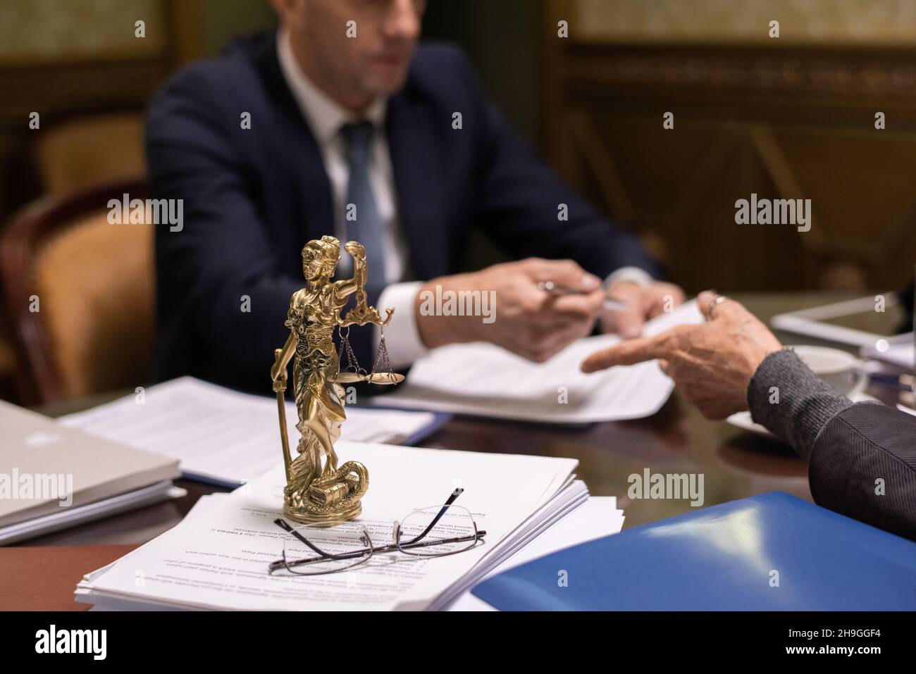 Statua di giustizia e occhiali su pila di documenti giuridici su tavola dove due avvocati discutere documenti Foto Stock