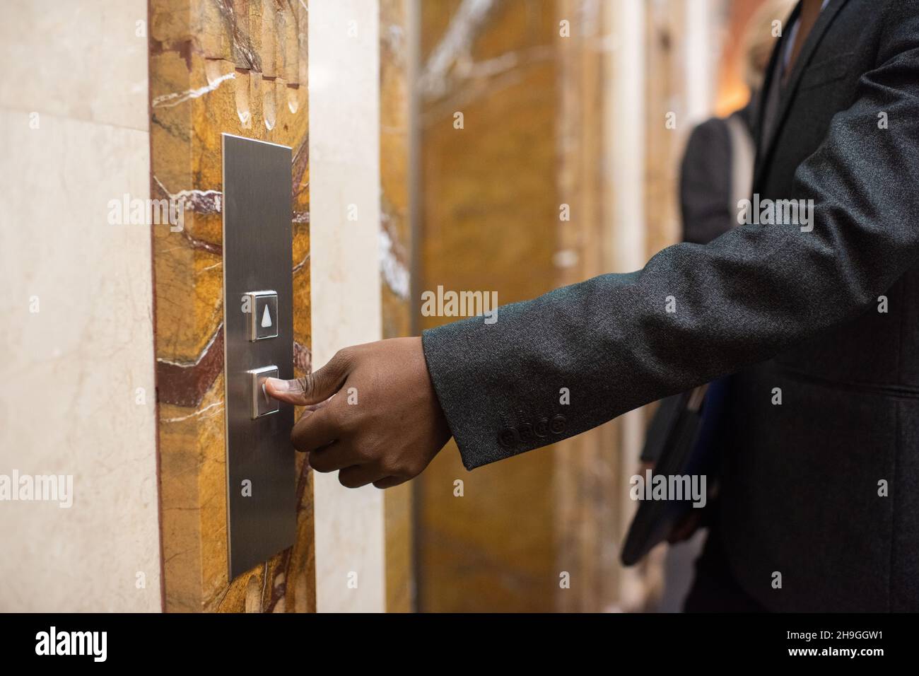 Mano di giovane uomo d'affari africano contemporaneo in abbigliamento formale premendo il pulsante per chiamare ascensore Foto Stock