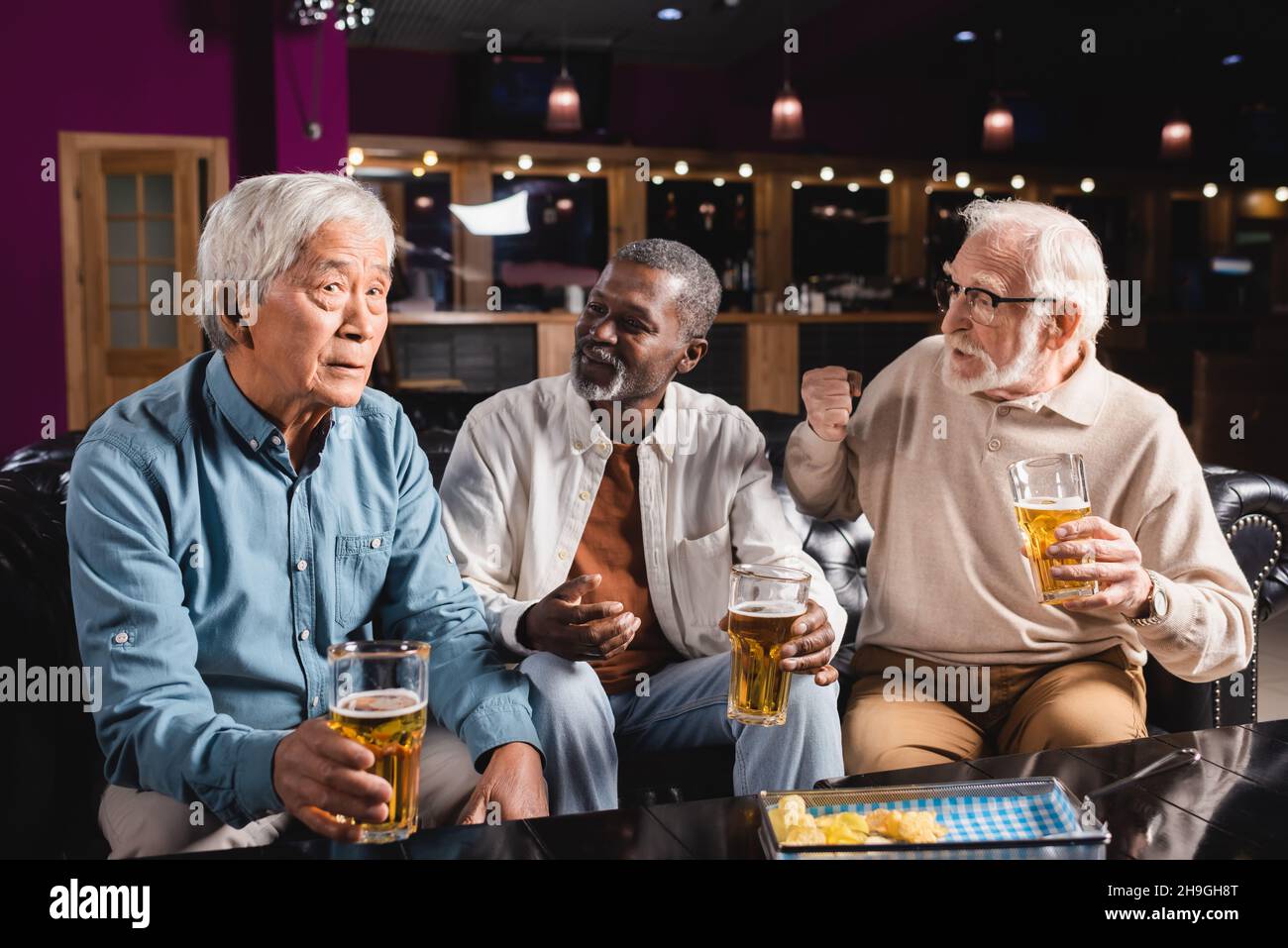 amici senior interrazziali gesturing mentre si parla con un amico asiatico in pub Foto Stock