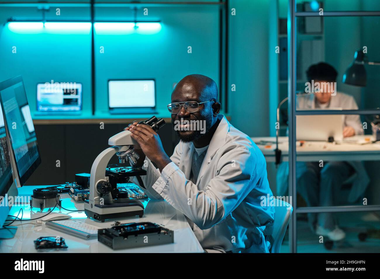 Giovane ricercatore di successo con microscopio seduto sul posto di lavoro in laboratorio scientifico Foto Stock