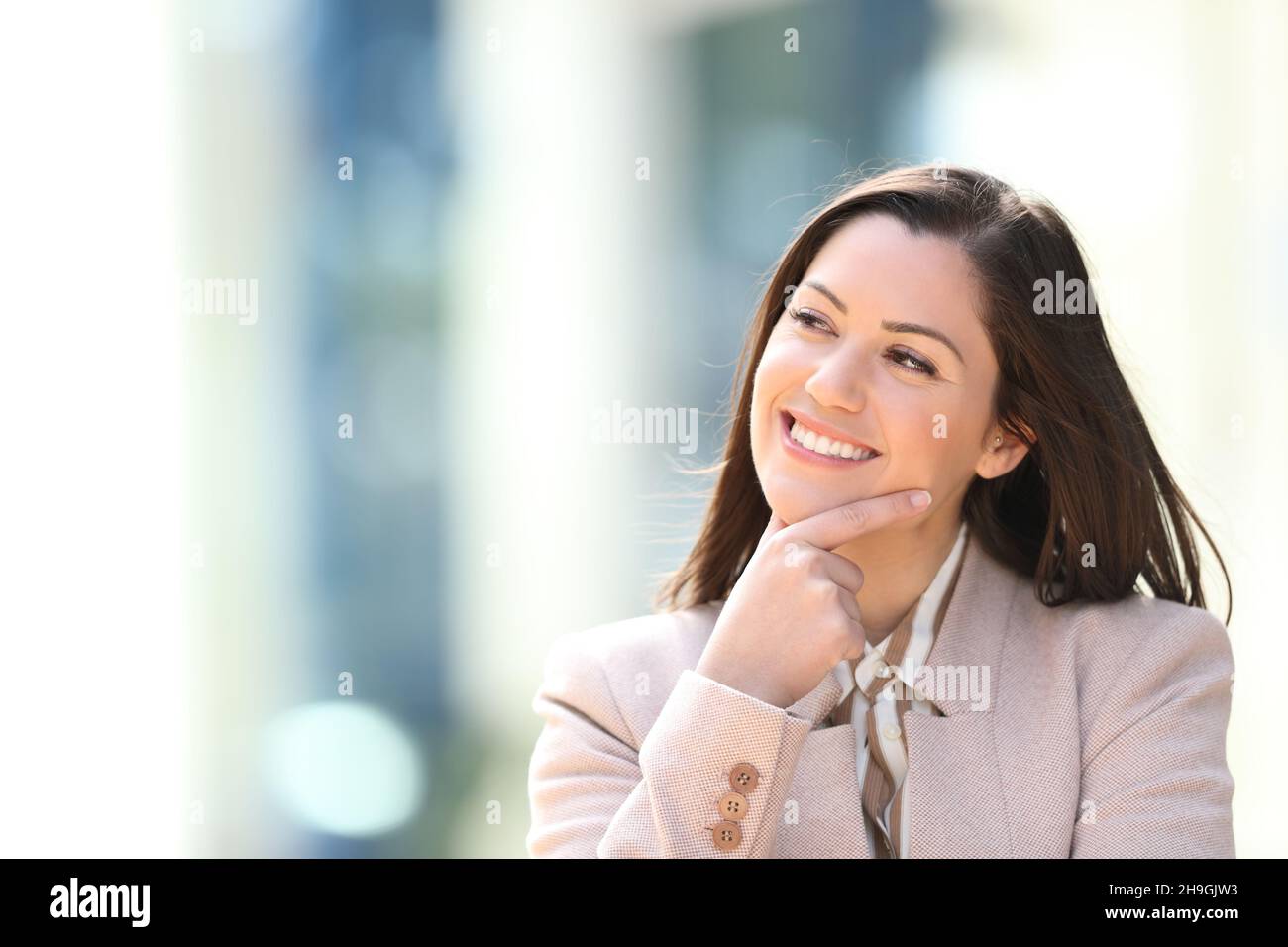 Donna d'affari felice che pensa guardando il lato all'aperto nella strada Foto Stock