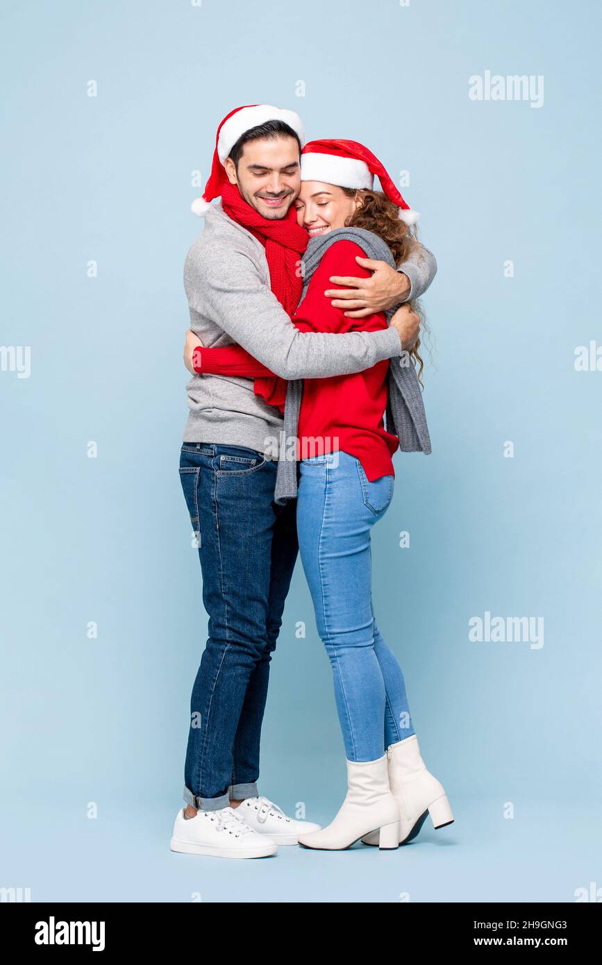 Ritratto a tutta lunghezza di felice coppia caucasica in abiti di Natale che si abbracciano a vicenda in blu chiaro isolato studio sfondo Foto Stock