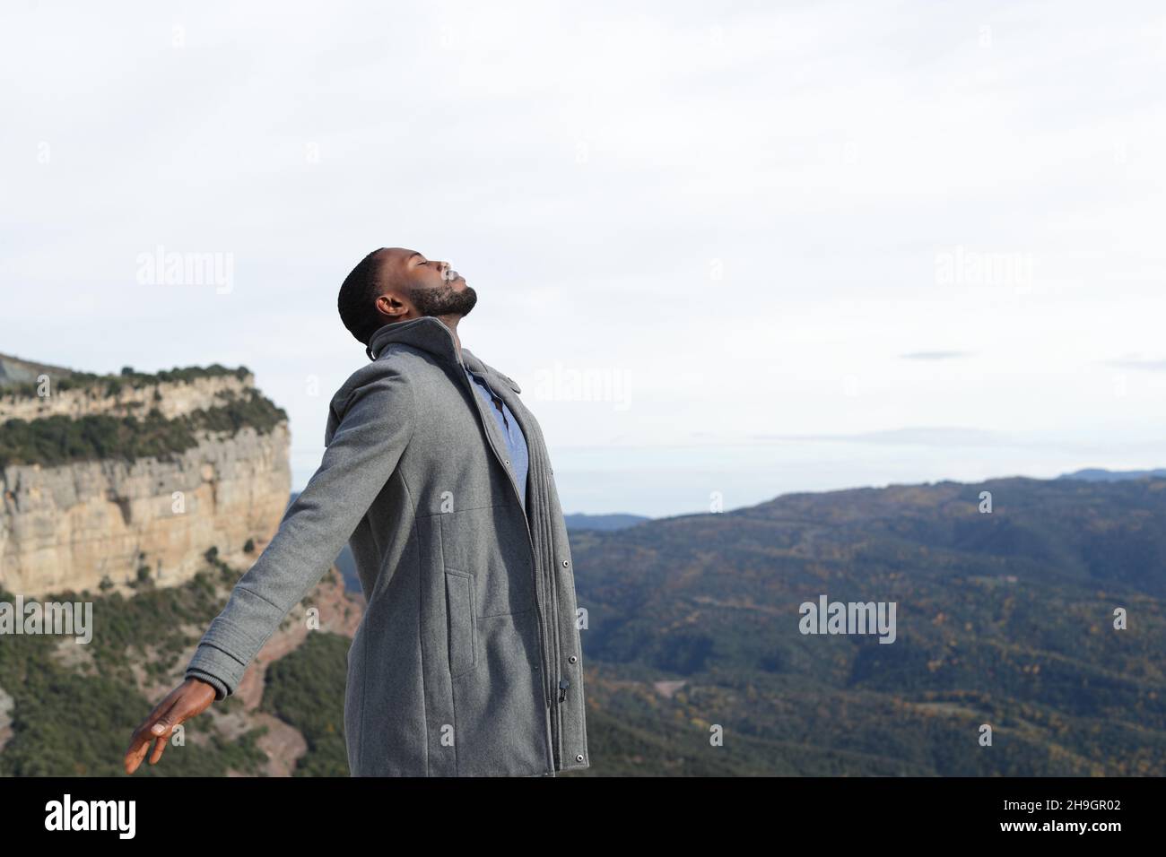 Uomo rilassato con pelle nera respirando aria fresca indossando giacca in inverno in natura Foto Stock