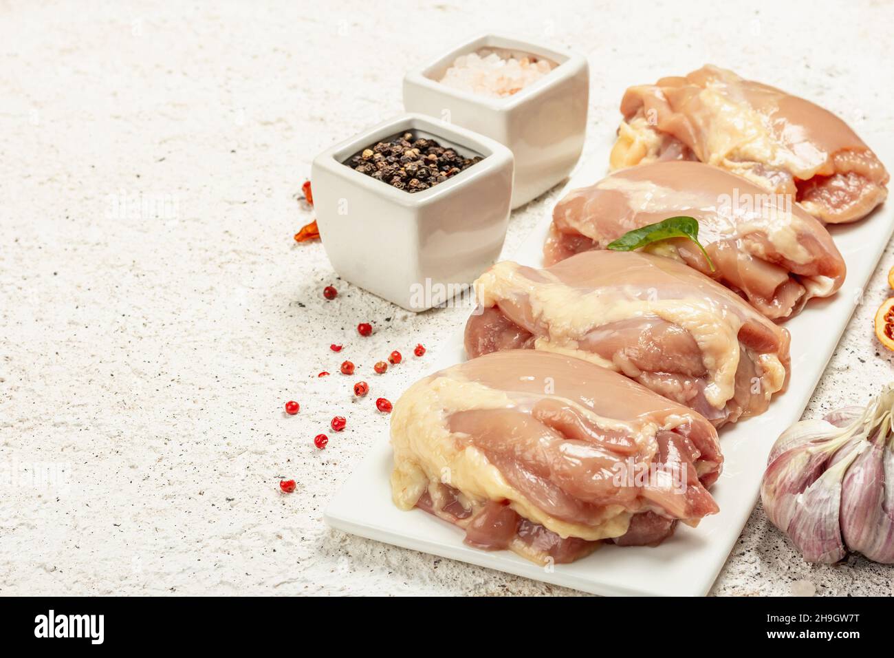 Coscia di pollo cruda senza ossa o pelle. Un ingrediente utile per preparare cibi sani, spezie, aglio. Sfondo di stucco chiaro, spazio di copia Foto Stock