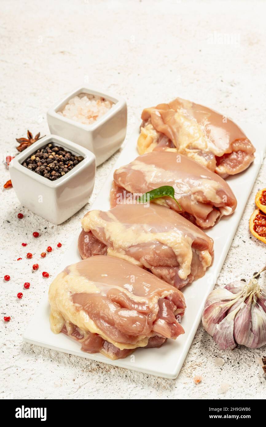 Coscia di pollo cruda senza ossa o pelle. Un ingrediente utile per preparare cibi sani, spezie, aglio. Fondo di stucco chiaro, primo piano Foto Stock