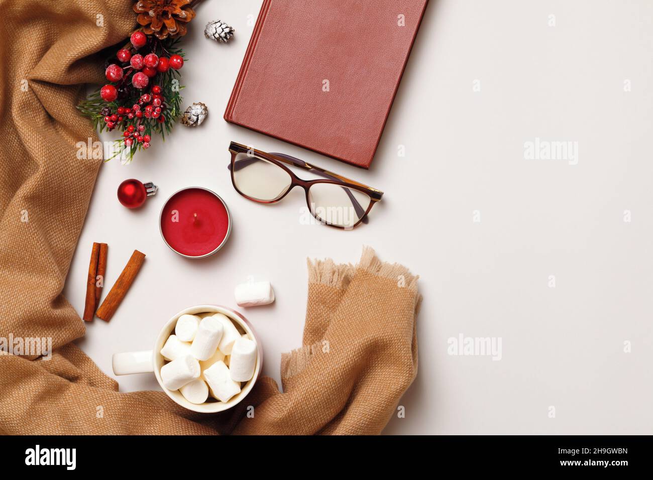 Sciarpa in cashmere beige con bicchieri da libro a candela in tazza marshmallow su sfondo grigio chiaro. Concetto di comfort invernale. Spazio di copia con vista dall'alto in posizione piana. Foto Stock