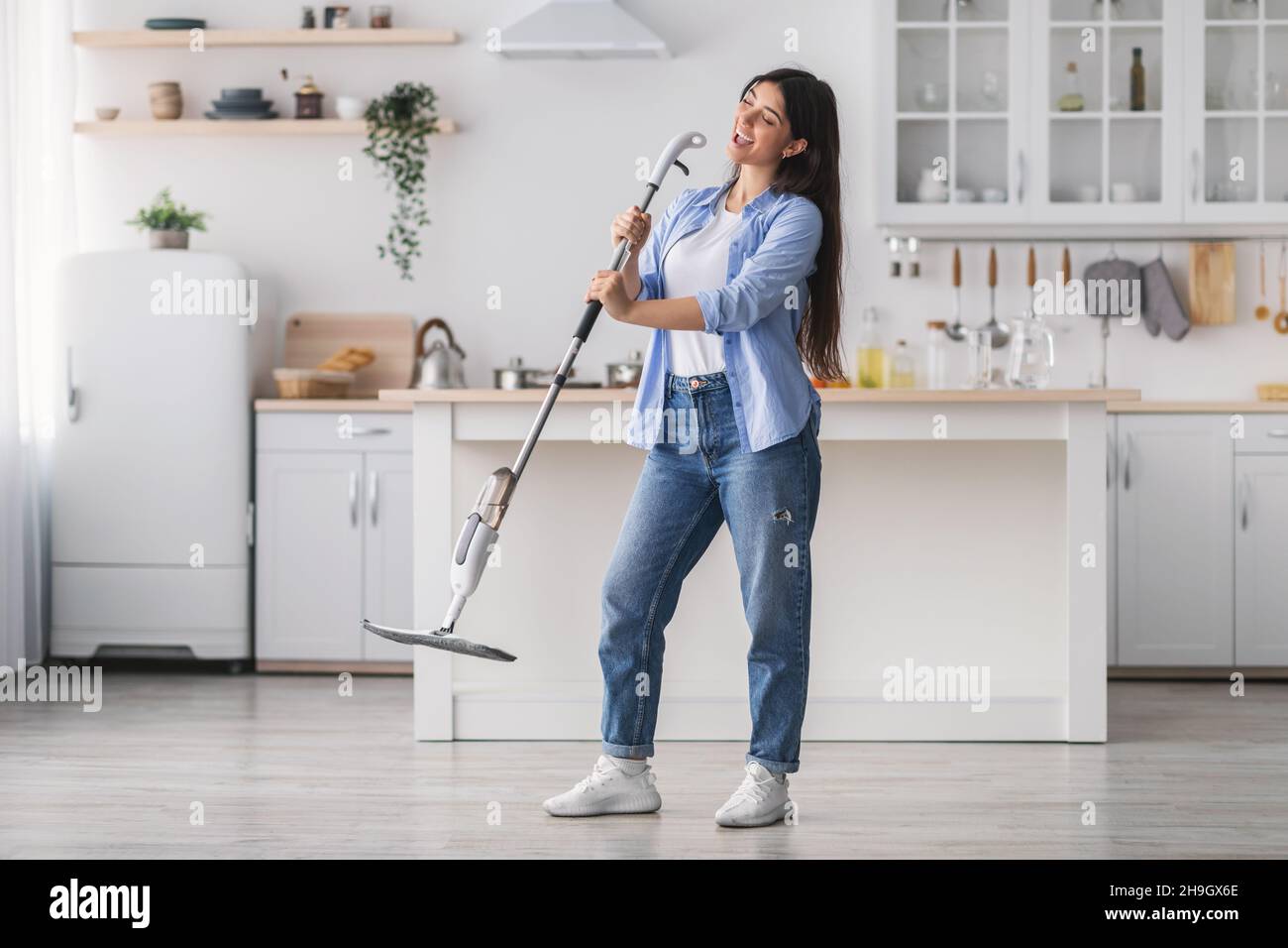 Donna allegra pulizia pavimento cantare tenendo mop in cucina Foto Stock