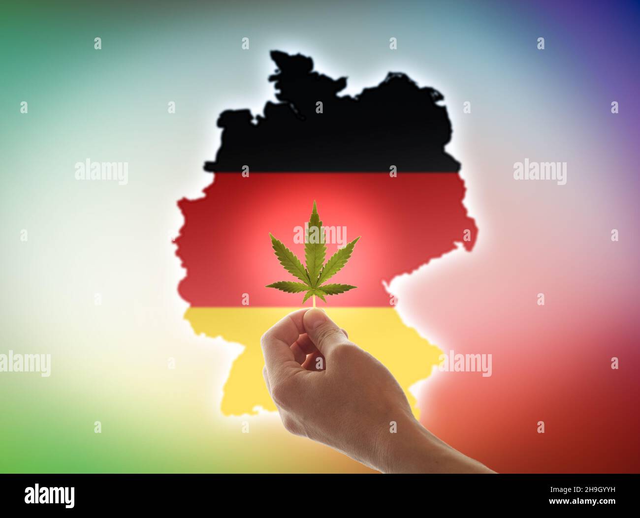 La mano di una donna tiene una foglia di cannabis sullo sfondo della bandiera tedesca. Il concetto di legalizzazione della marijuana in Germania. Foto Stock