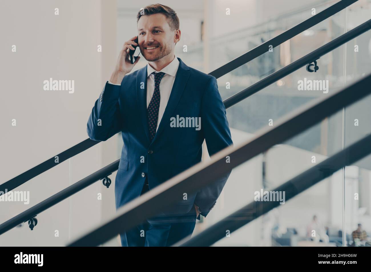 Bell'uomo d'affari europeo in elegante abito blu con conversazione mobile in ufficio Foto Stock