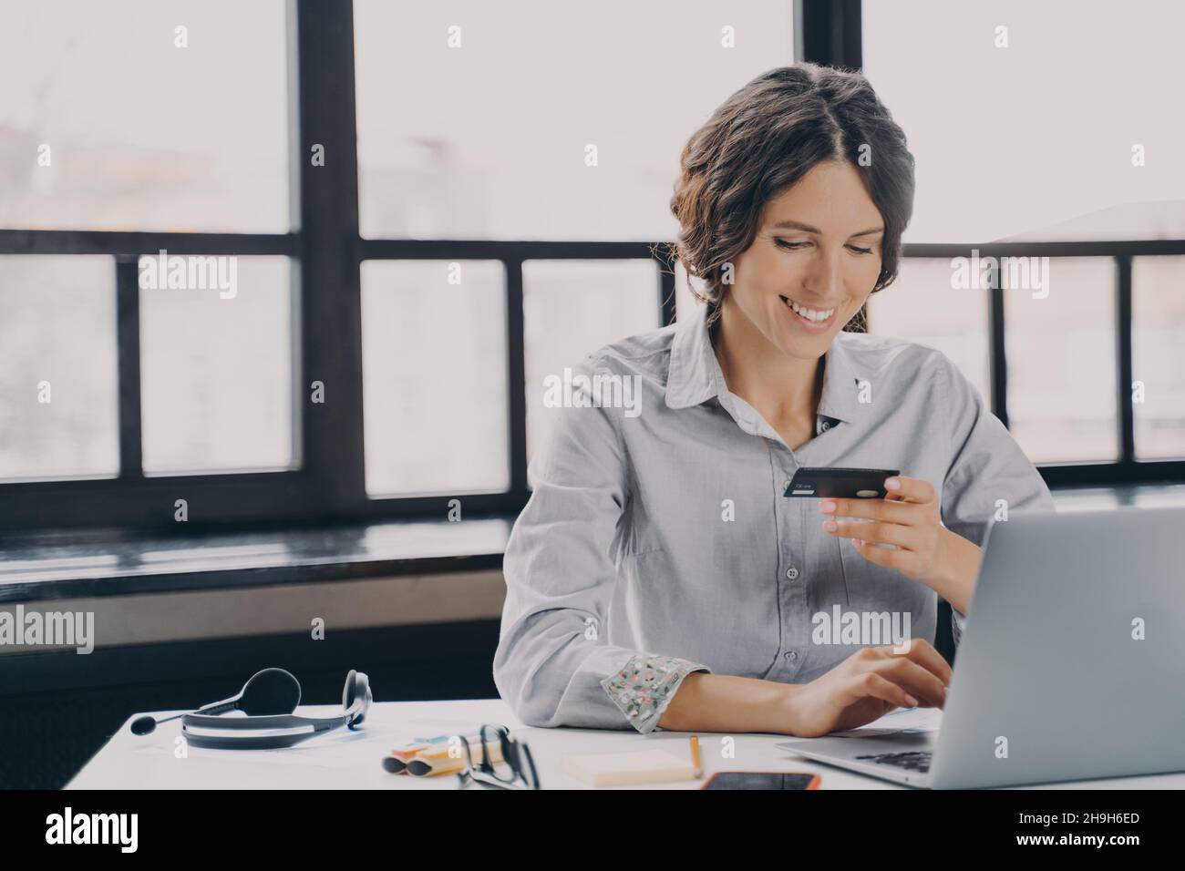 Felice dipendente italiano donna ufficio con carta di credito, facendo shopping online via laptop Foto Stock