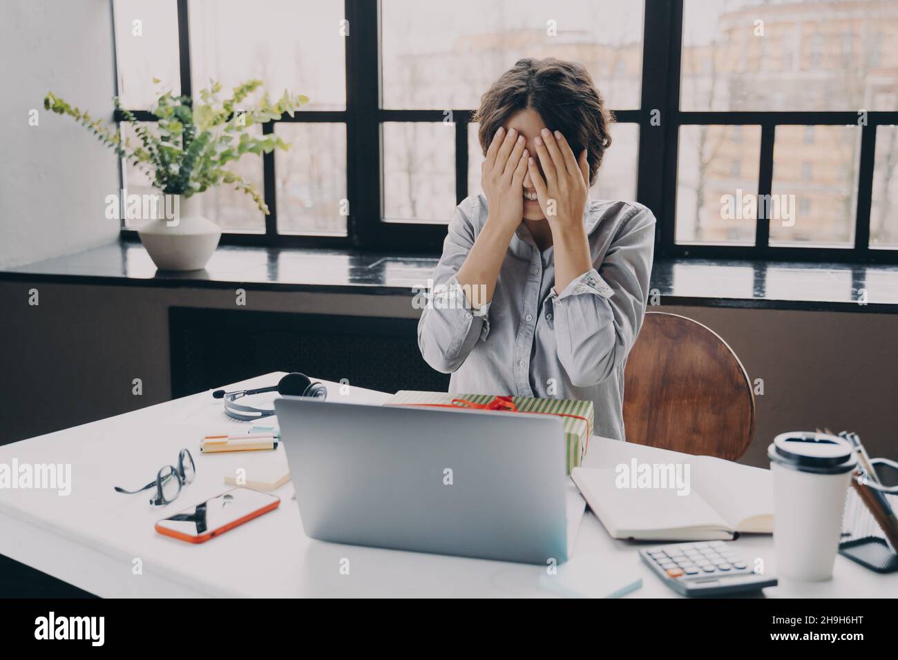 Curioso dipendente ufficio donna che copre gli occhi con le mani, mentre ottenere x-mas presenti al lavoro Foto Stock