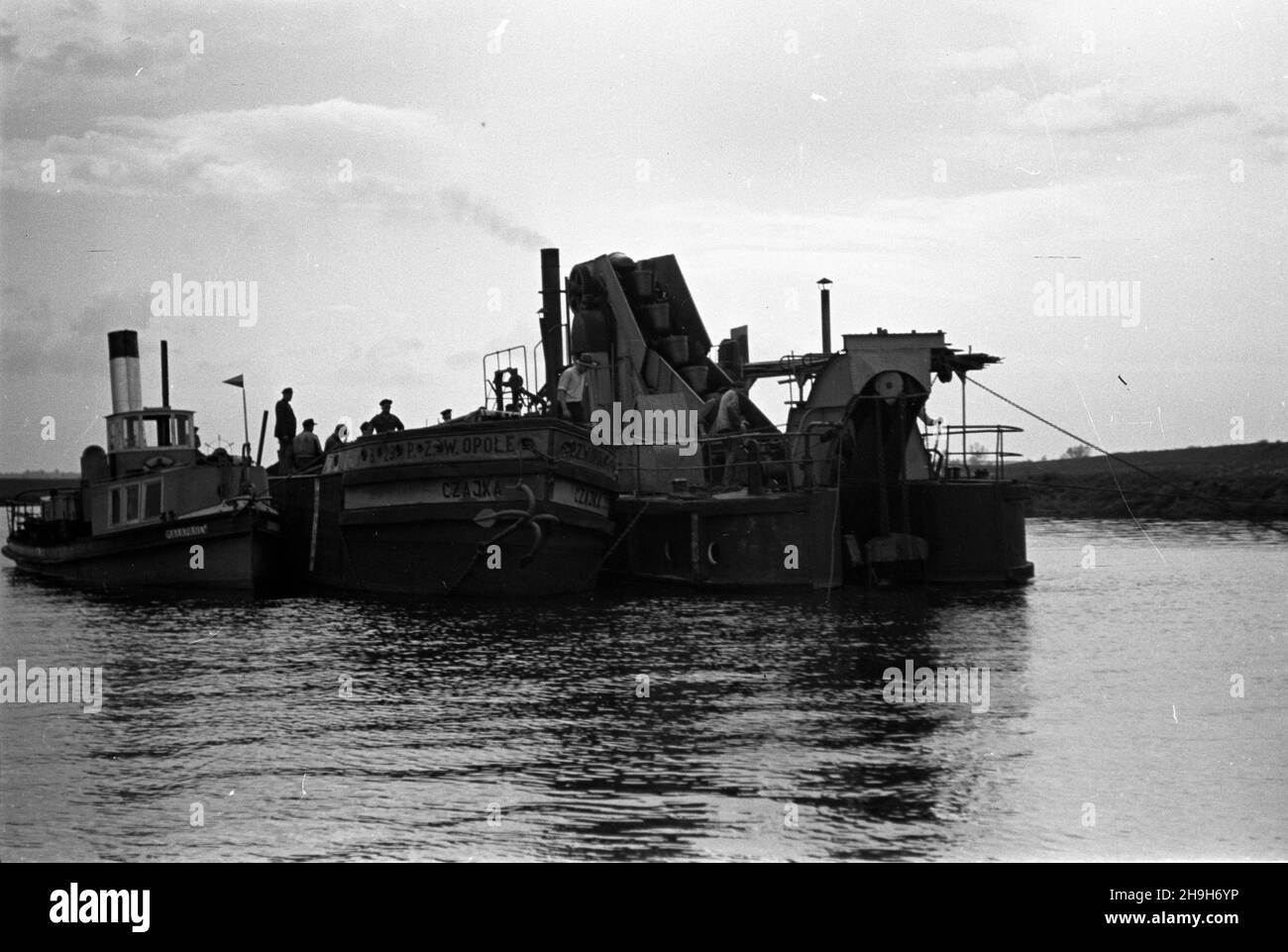 Polska, 1948-07. Pracuj¹cy na Odrze rzeczny zespó³ Transportowy i pog³êbiarka. NZ. pog³êbiarka (P) ³aduje wydobyty piach na barkê Czajka, któr¹ poci¹gnie holownik parowy Ma³apanew (L). mw PAP Dok³adny dzieñ wydarzenia nieustalony. Polonia, luglio 1948. Un'unità di trasporto fluviale e un drago che lavorano sul fiume Odra. Nella foto: Un drago (a destra) che carica la sabbia estratta sulla chiatta Czajka per essere trainata dal rimorchiatore Malapanew alimentato a vapore (a sinistra). mw PAP Foto Stock