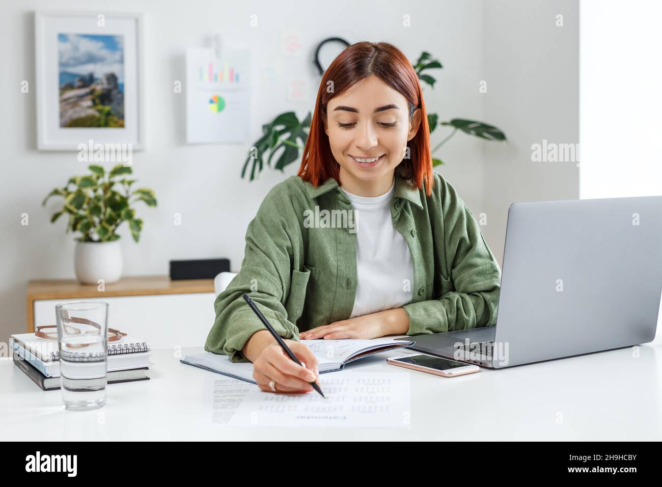Donna che lavora da remoto a casa con un computer portatile. Giovane donna d'affari che pianifica il suo tempo. Concetto di business online, freelance, home Office e tel Foto Stock