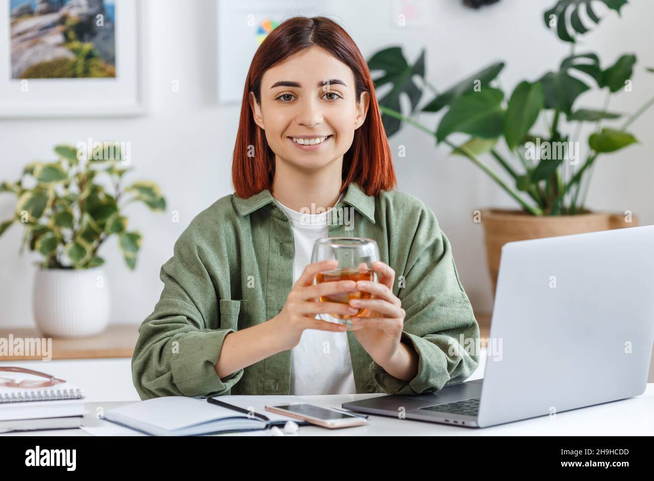 Ritratto di una giovane donna che lavora a casa con un computer portatile. Donna d'affari rilassata che tiene una tazza di tè. Concetto di business o comunicazione online, freelance, Foto Stock