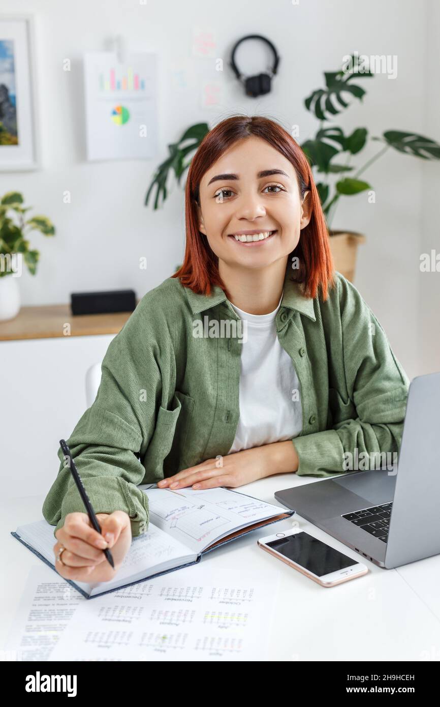 Donna che lavora da remoto a casa con un computer portatile. Giovane donna d'affari che pianifica il suo tempo. Concetto di business online, freelance, home Office e tel Foto Stock