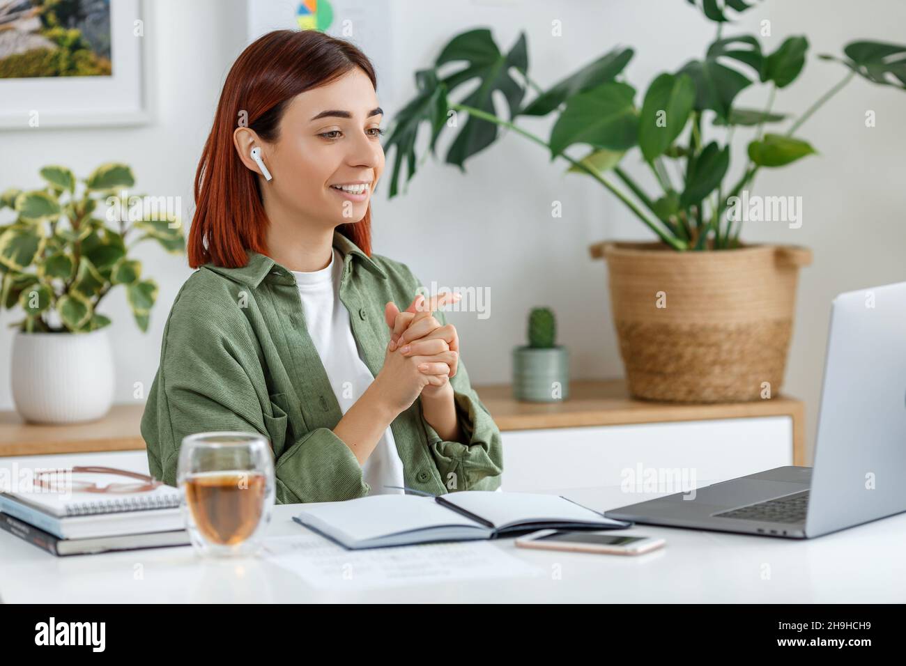 Donna che lavora in remoto a casa con un computer portatile. Giovane donna d'affari che parla con gli auricolari wireless. Concetto di business online o di comunicazione, freelance Foto Stock