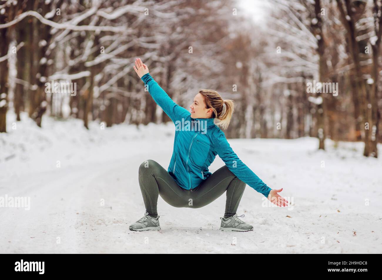 Indossa uno sport sportivo che si accoccola in una posa di yoga in natura quando il clima è nevoso. Fitness all'aperto, neve, freddo, yoga invernale Foto Stock