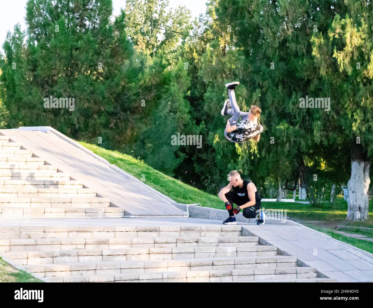 Giovane uomo che fa pericoloso salto somersault salto su un altro uomo accoccolato sui gradini del parco. Foto Stock