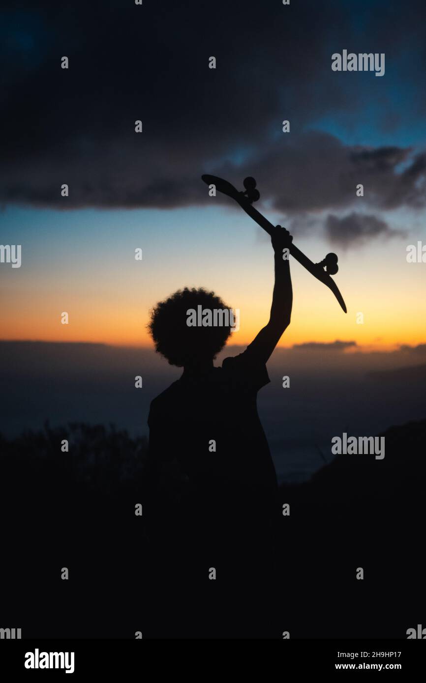 Giovane afro che tiene uno skateboard durante il tramonto. Foto Stock