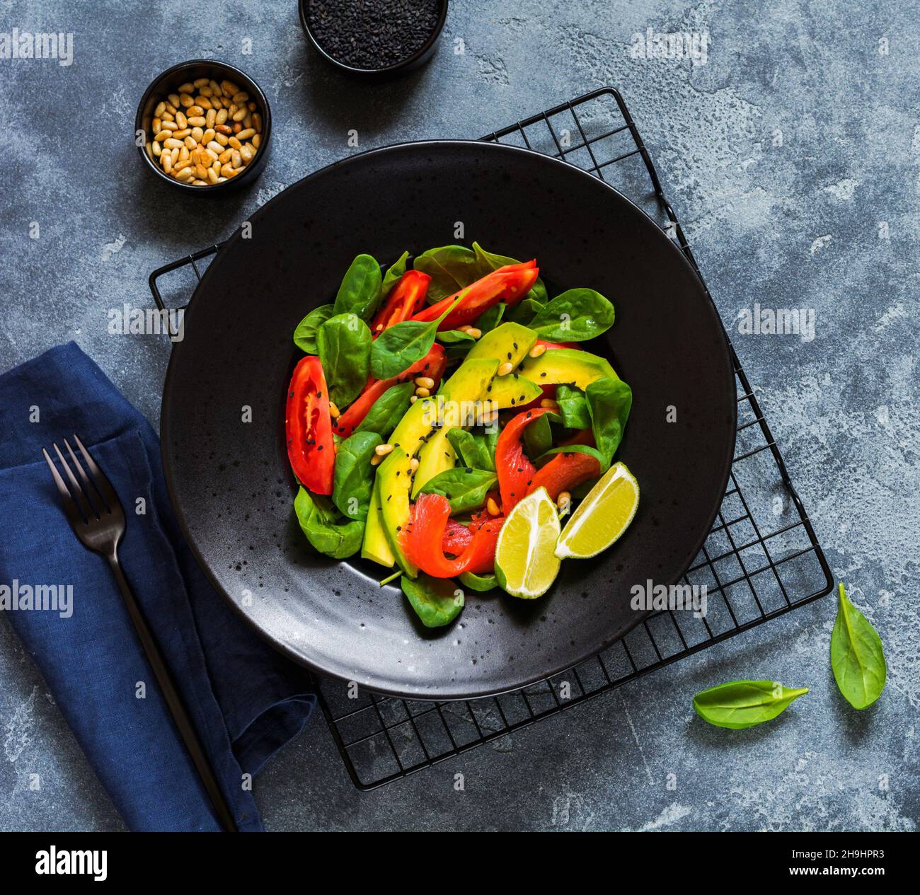 Avocado, salmone, spinaci, pomodoro, pinoli e insalata di sesamo nero in un piatto di ceramica nera. Vista dall'alto. Foto Stock