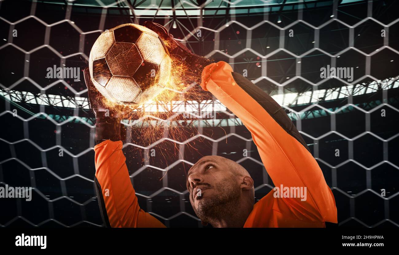 Primo piano di una scena calcistica durante la partita notturna con un portiere che cerca di catturare una palla ardente Foto Stock
