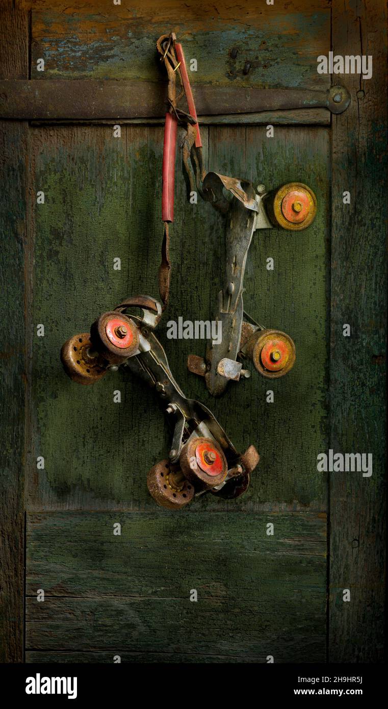 Coppia di vecchi pattini a rotelle per bambini arrugginiti appesi su una vecchia porta di legno. Foto Stock