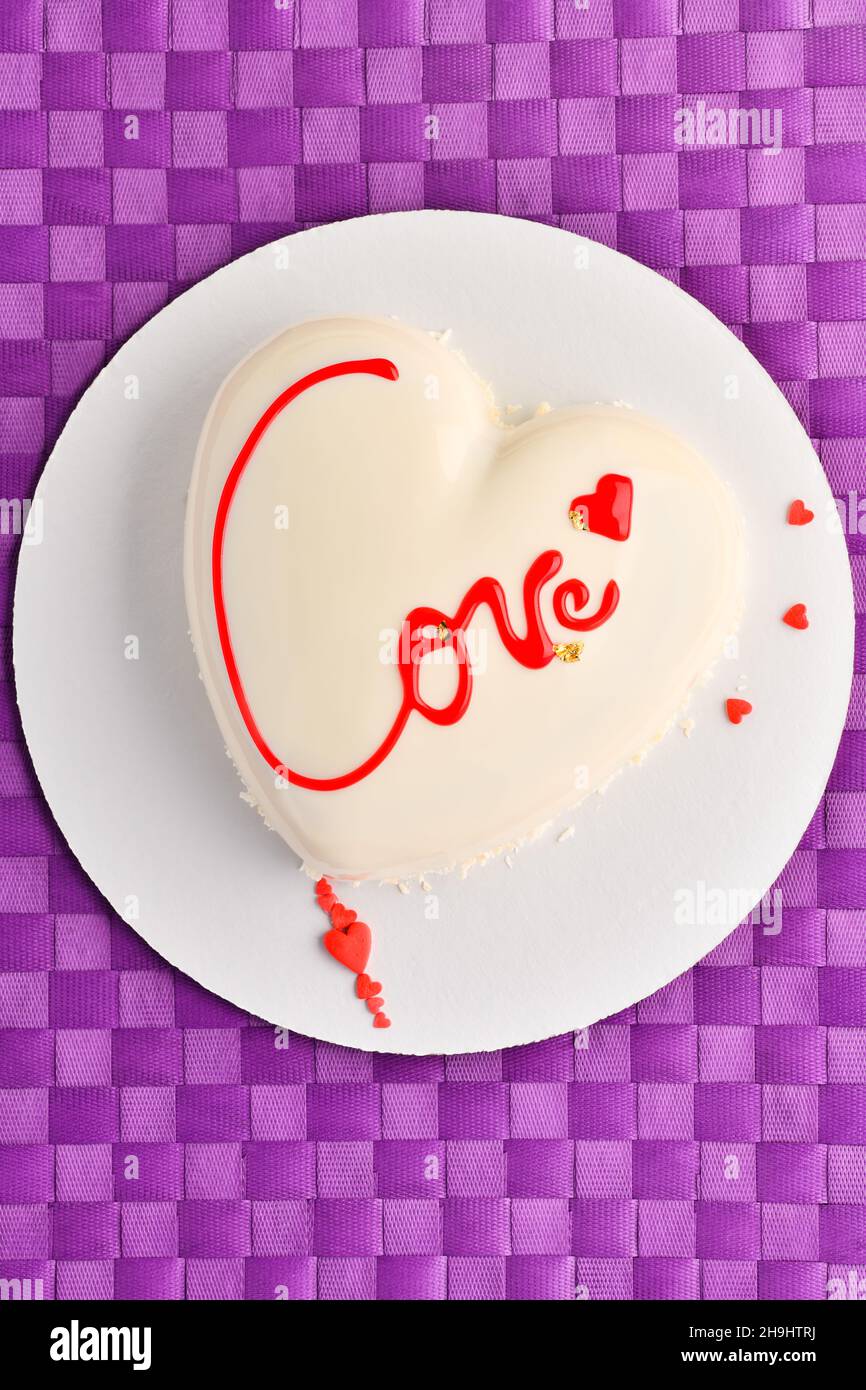 San Valentino sfondo per panetteria, pasticceria. Torta di mousse bianca a forma di cuore con l'iscrizione Love su sfondo viola Foto Stock