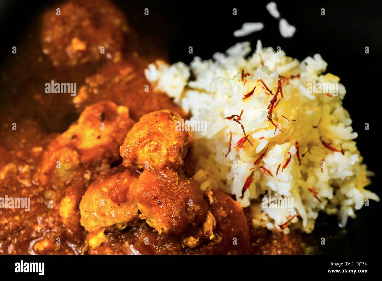 Particolare di curry di pollo in salsa piccante (in stile madras) e riso basmati con zafferano su sfondo nero, closeup. Cucina indiana tradizionale Foto Stock