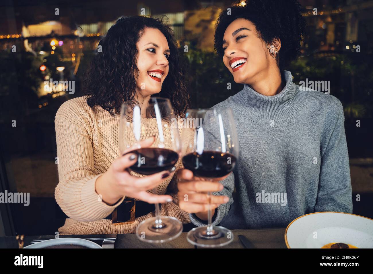 Coppia multirazziale di giovani migliori amici che festeggiano la tostatura con vino rosso - girlfriends multiculturali che accecano i vini al ristorante Foto Stock