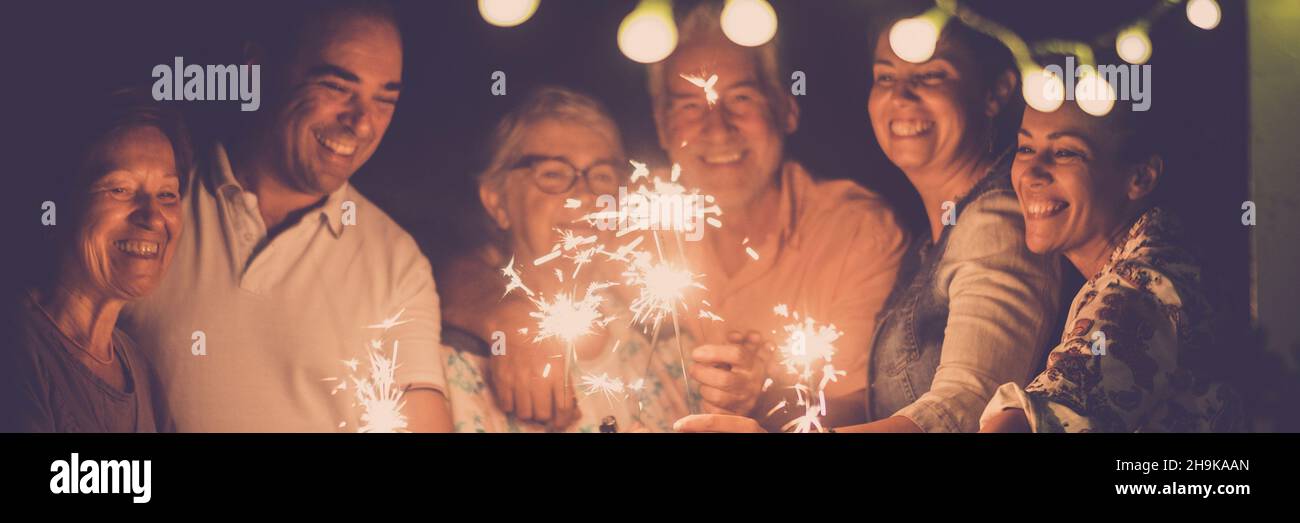 Gruppo di persone festeggiano con scintilla in amicizia. La famiglia con uomini e donne si divertono nella notte festeggiando l'anno nuovo o compleanno in testa banner Foto Stock