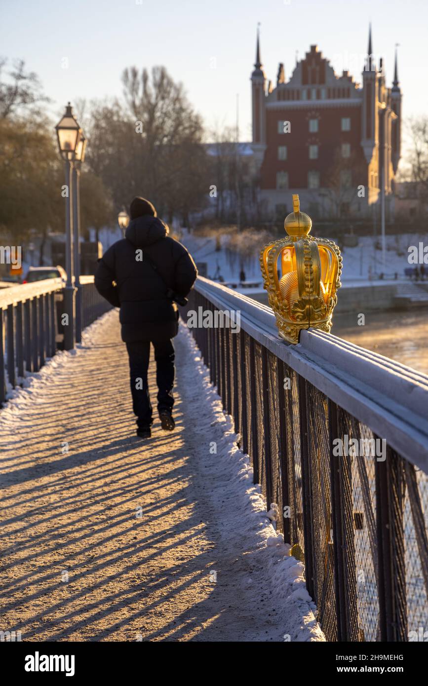Stoccolma in inverno. Persone che camminano sul ponte con una corona dorata su Skeppsholmsbron con Strandhagen sullo sfondo. Foto Stock