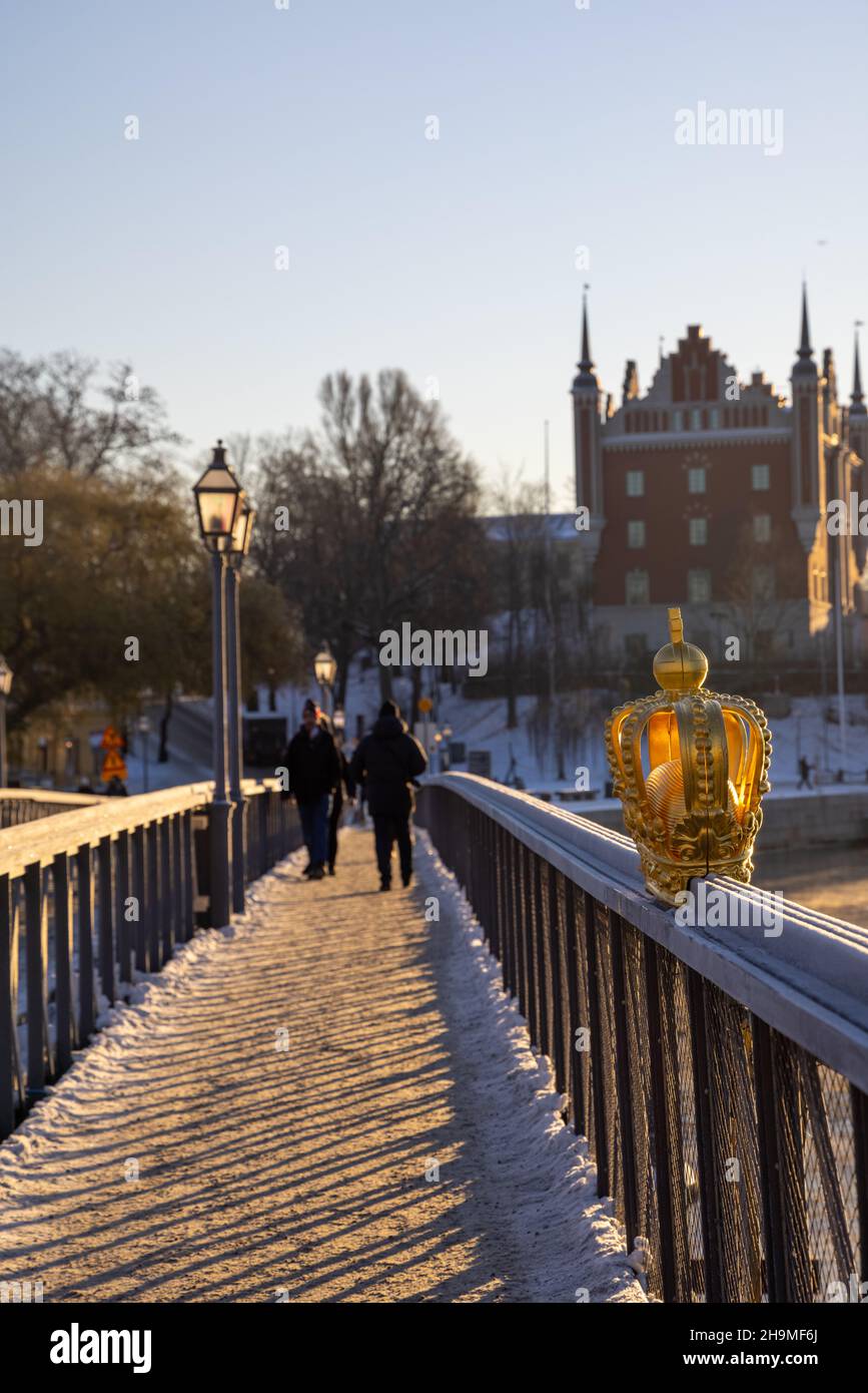 Stoccolma in inverno. Persone che camminano sul ponte con una corona dorata su Skeppsholmsbron con Strandhagen sullo sfondo. Foto Stock