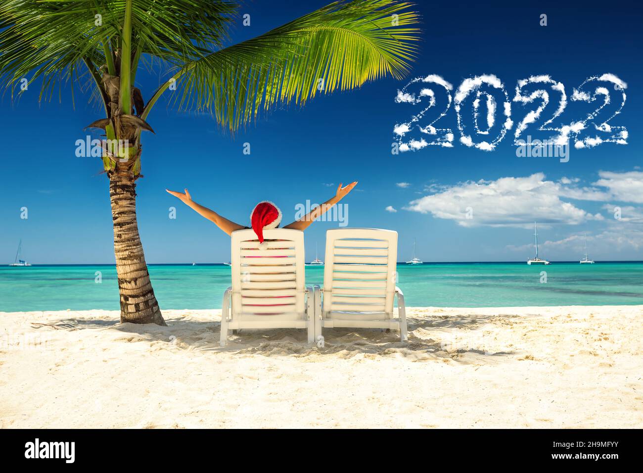 2022 concetto di nuovo anno con donna in cappello di babbo natale rilassante sulla spiaggia tropicale. Vacanza di nuovo anno sull'isola. Foto Stock