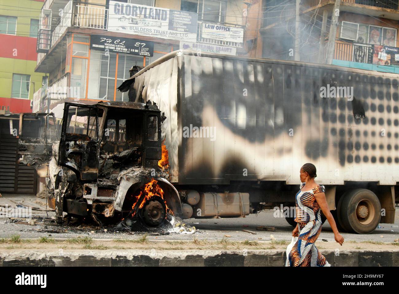 Lagos, Nigeria, 7 dicembre 2021. Una donna cammina oltre i resti del camion di consegna che ha ucciso alcuni studenti di ritorno dalla scuola Grammar School, Ojodu, Lagos, Nigeria. Mentre il testimone oculare ha detto che almeno 17 alunni sono morti, la polizia ha confermato tre morti, 12 feriti nell'incidente di martedì. Foto di Adekunle Ajayi Foto Stock