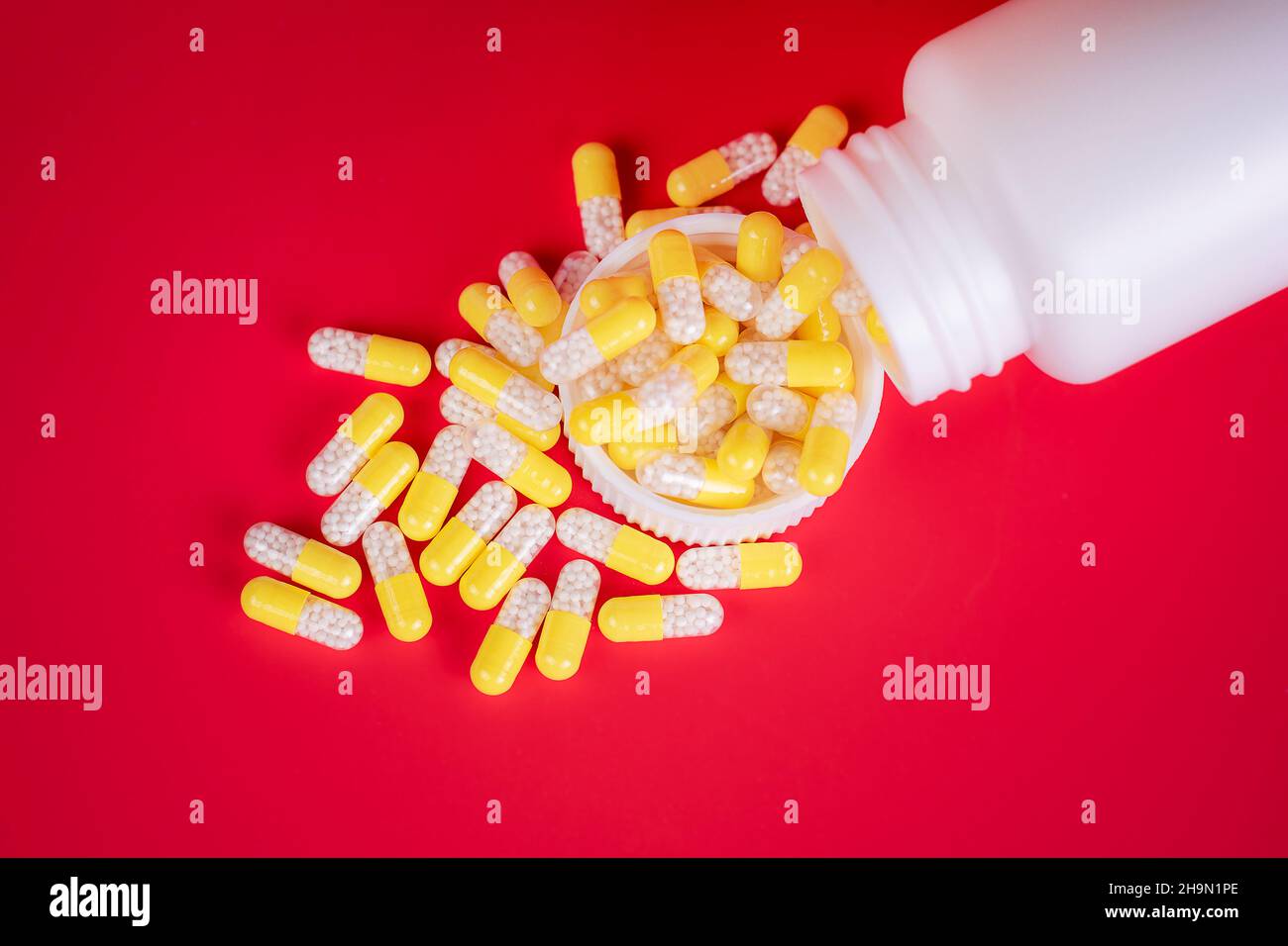 Concetto di medicina. Capsule gialle sparse dal flacone con prescrizione medica. Lo sfondo è di colore rosso, con spazio per la scrittura. Foto studio. Foto Stock