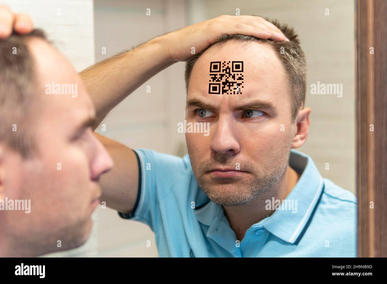 Un uomo con un'espressione stupida guarda il suo codice qr sulla testa. Il concetto di scalpellare la popolazione. Giovane con un codice qr sulla fronte. glo Foto Stock