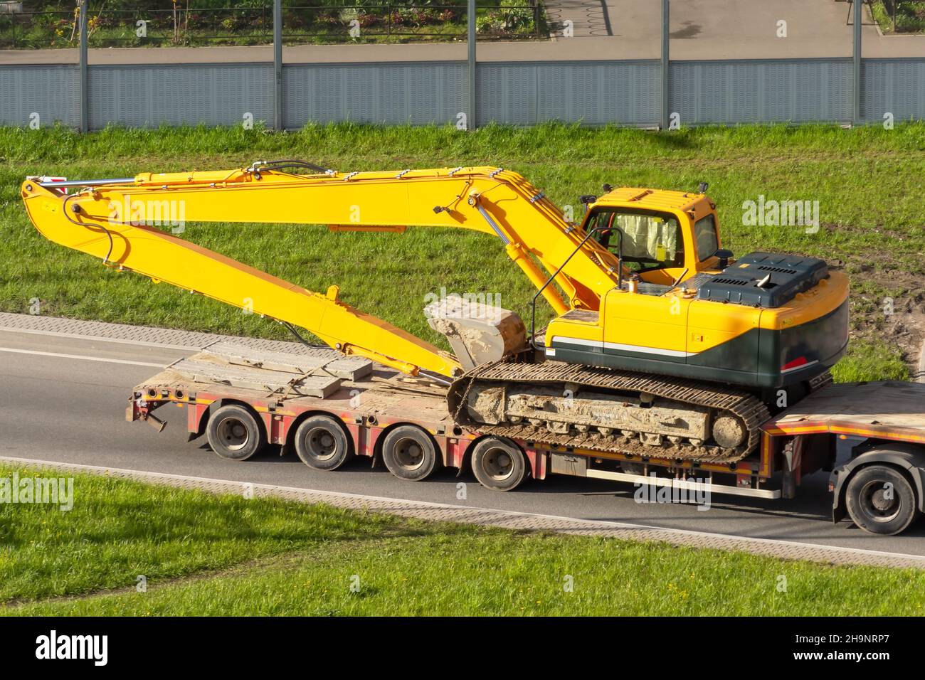 Escavatore pesante caricato sul rimorchio a pianale ribassato tramite rampa posteriore Foto Stock