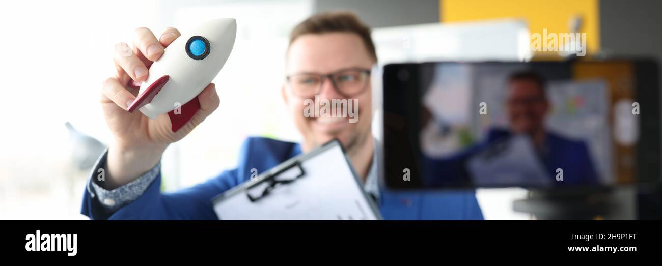 Maschio blogger tiene razzo e grafico con indicatori finanziari e registra video di formazione Foto Stock