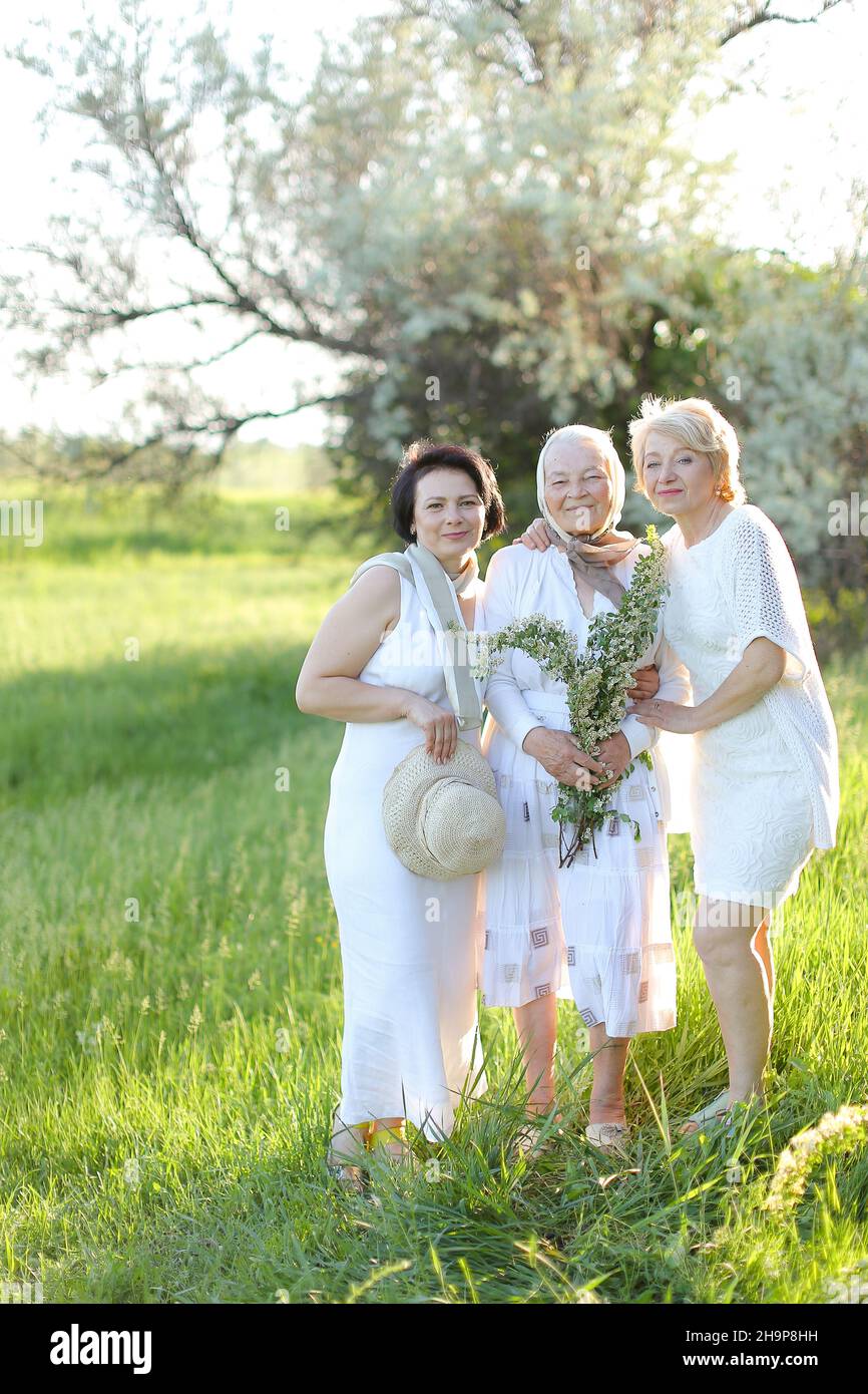 Due figlie in piedi con la vecchia madre fuori e indossare abiti bianchi. Foto Stock