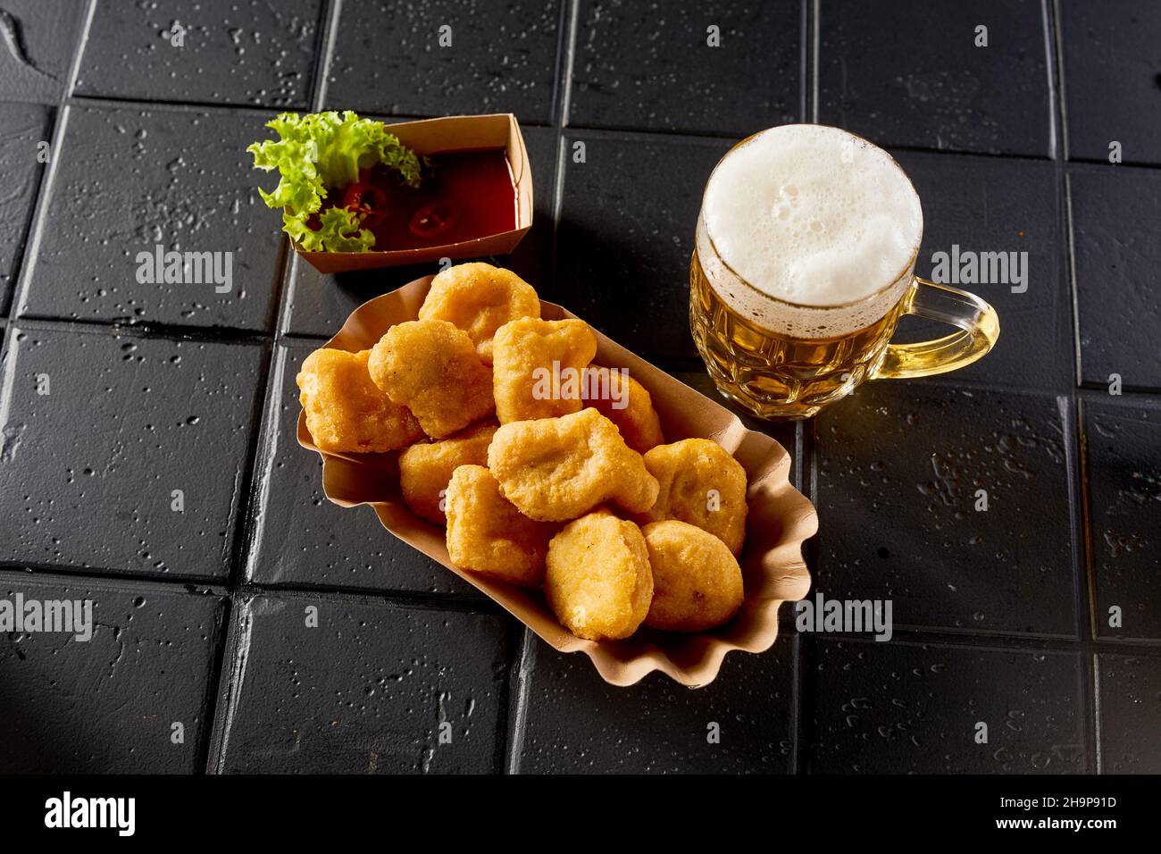 Angolo elevato di deliziosi pepite di pollo caldo e bicchiere di birra alcolica con schiuma posta sul tavolo nero Foto Stock