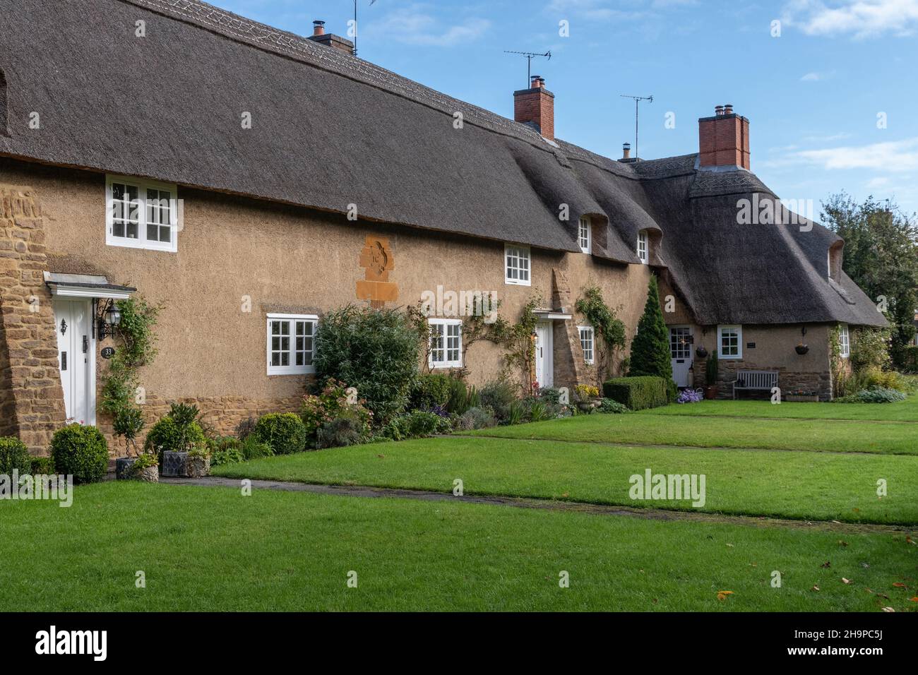 Una pittoresca fila di cottage con il tetto di paglia progettato da Sir Edwin Luytens nel villaggio di Ashby St partitari, Northamptonshire, Regno Unito Foto Stock