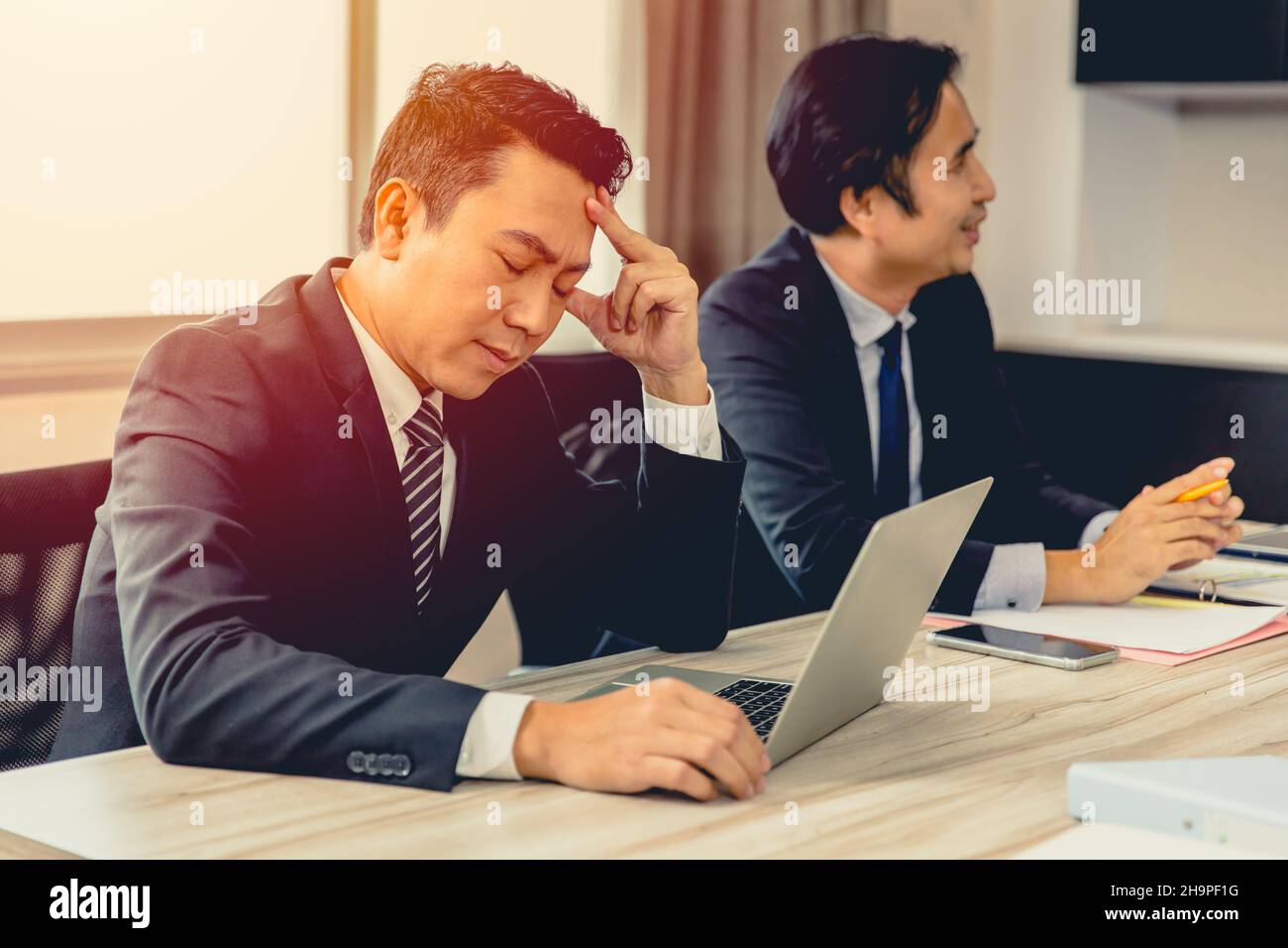 Un uomo d'affari si sente stanco di mal di testa con un amico felice nella sala riunioni d'affari. Foto Stock