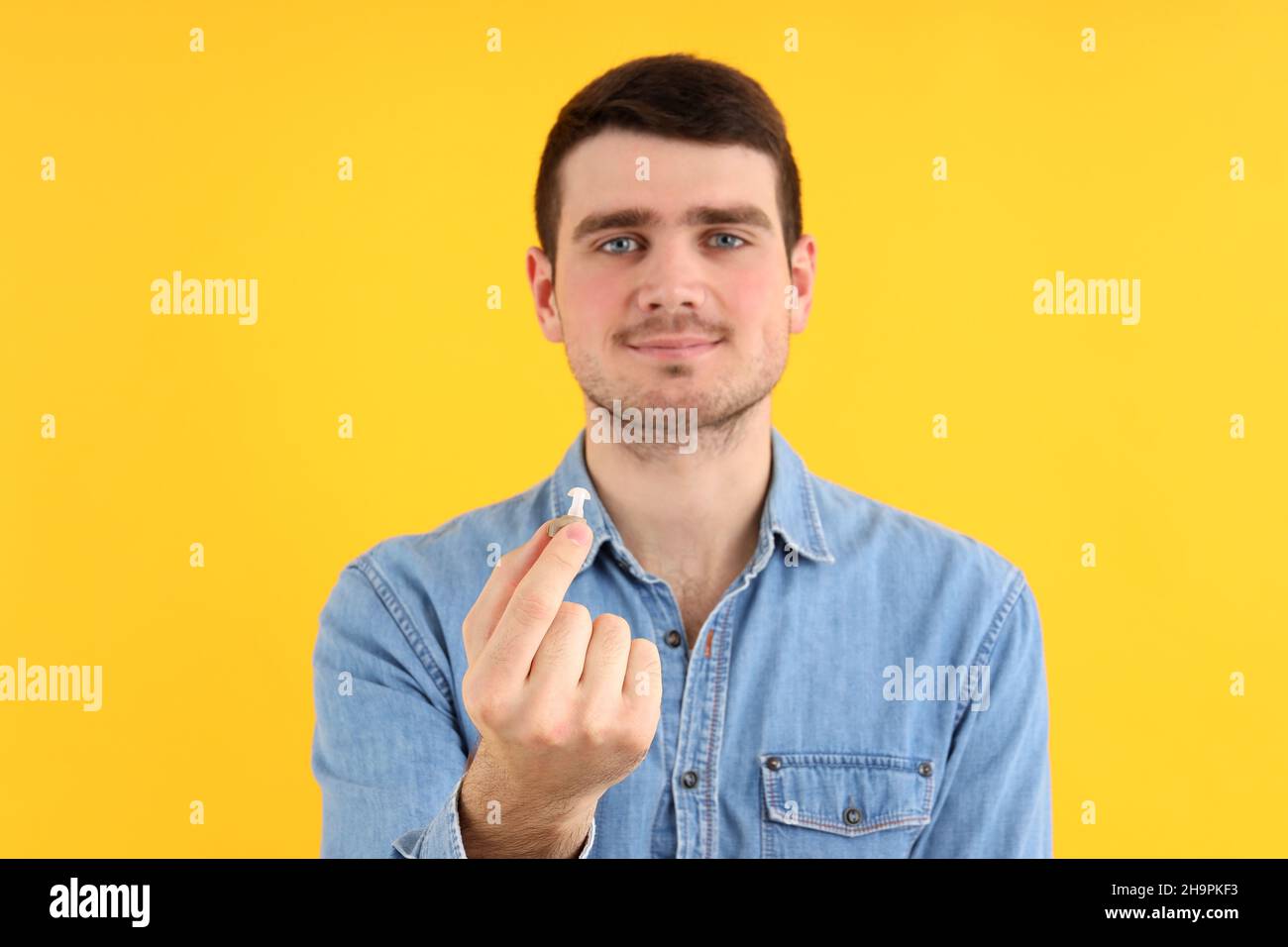 Il giovane uomo tiene gli apparecchi acustici su sfondo giallo Foto Stock
