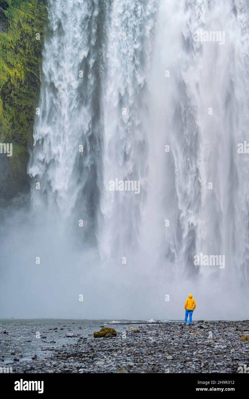 Enorme cascata dietro una persona, cascata di Skogafoss, Islanda del Sud, Islanda Foto Stock