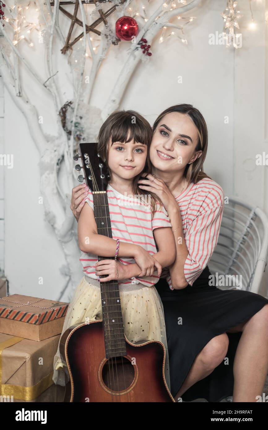 Foto di famiglia studio di Natale. Foto di Capodanno della famiglia felice. Bella madre e figlia carina nella stessa t-shirt seduta con chitarra. Foto Stock