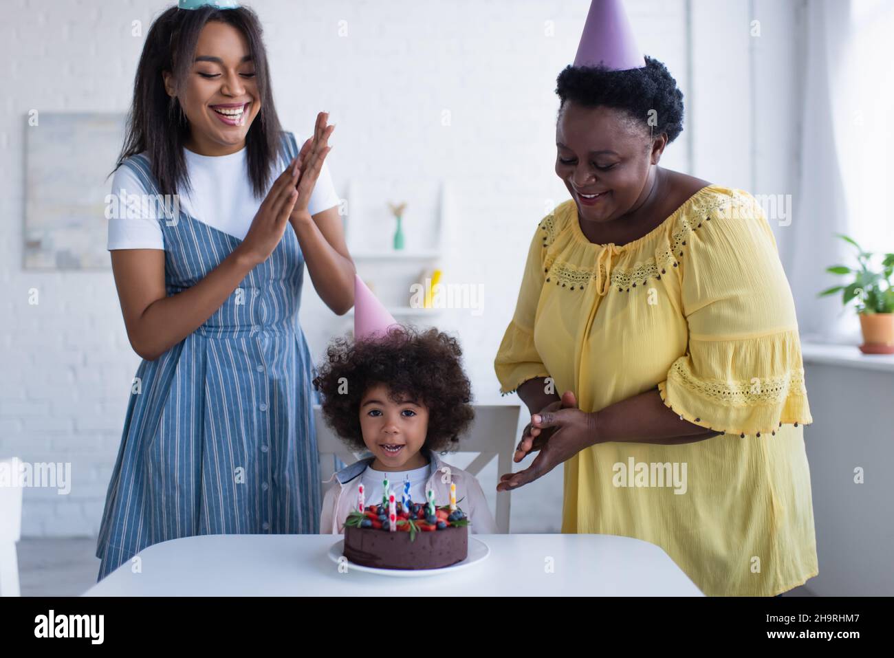 allegre donne afroamericane che stringono le mani vicino alla bambina e alla torta di compleanno Foto Stock