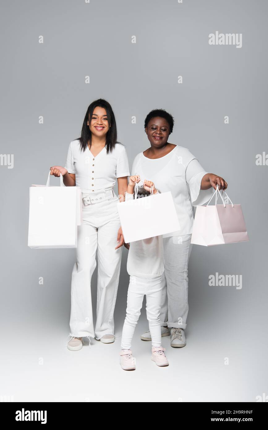 felice african american donne e bambino bambino con borse shopping bianco su grigio Foto Stock
