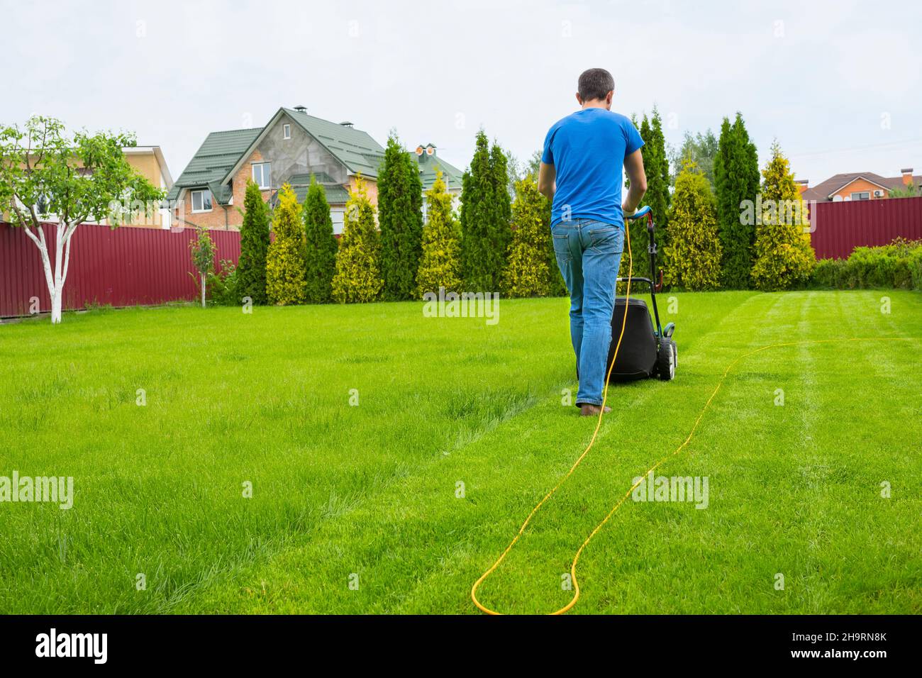 Un giardiniere con un rasaerba sta tagliando l'erba nel giardino nel cortile della casa. Foto Stock