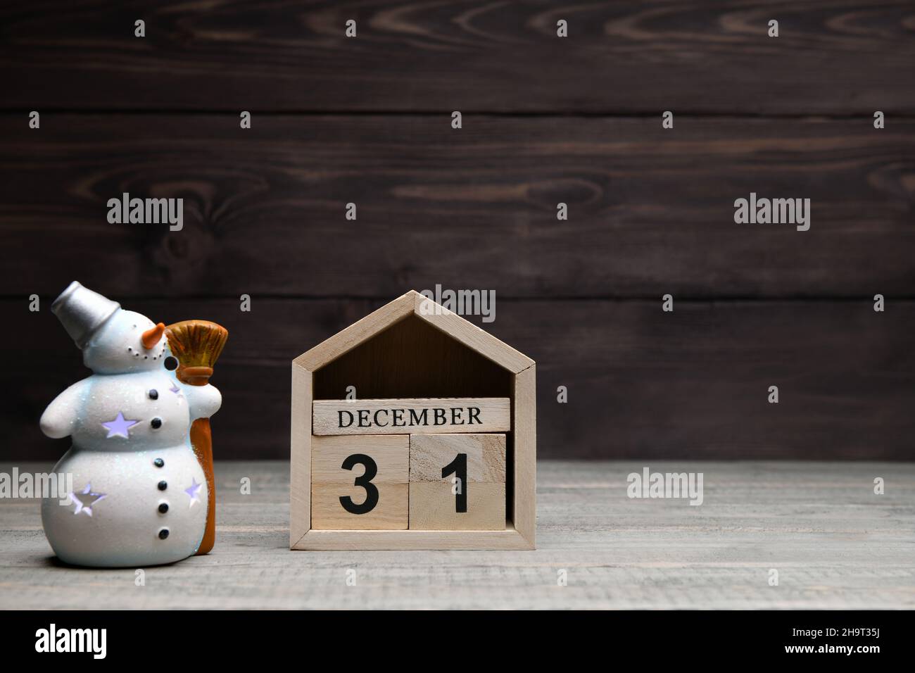 Decorazioni natalizie su sfondo ligneo: Cubetti di legno con i numeri dicembre 31 e un pupazzo di neve brillante. Messa a fuoco selettiva Foto Stock