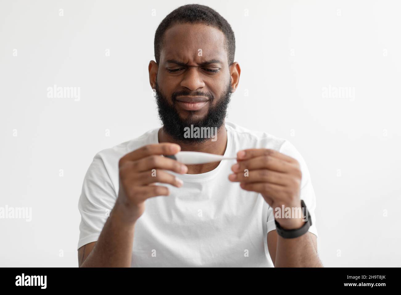 Ritratto di uomo senza happy millennial nero bearded guardare termometro con alta temperatura su sfondo bianco parete Foto Stock